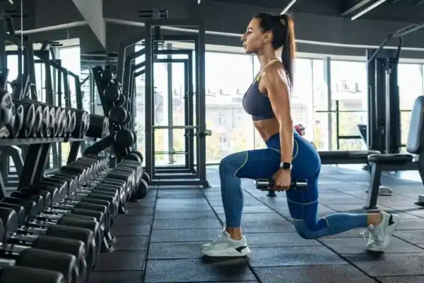 Fit Woman Doing A Dumbbell Lunge In The Gym
